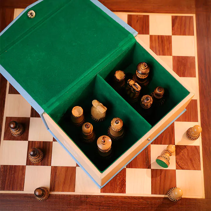 Wooden chess pieces in a green box on a checkered wooden surface