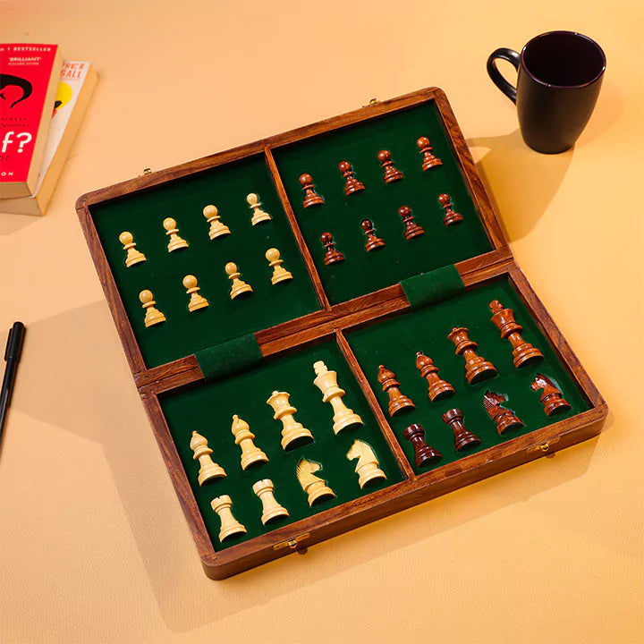 Wooden chess set with pieces on a green felt surface, placed on a beige surface with a book and mug in the background.